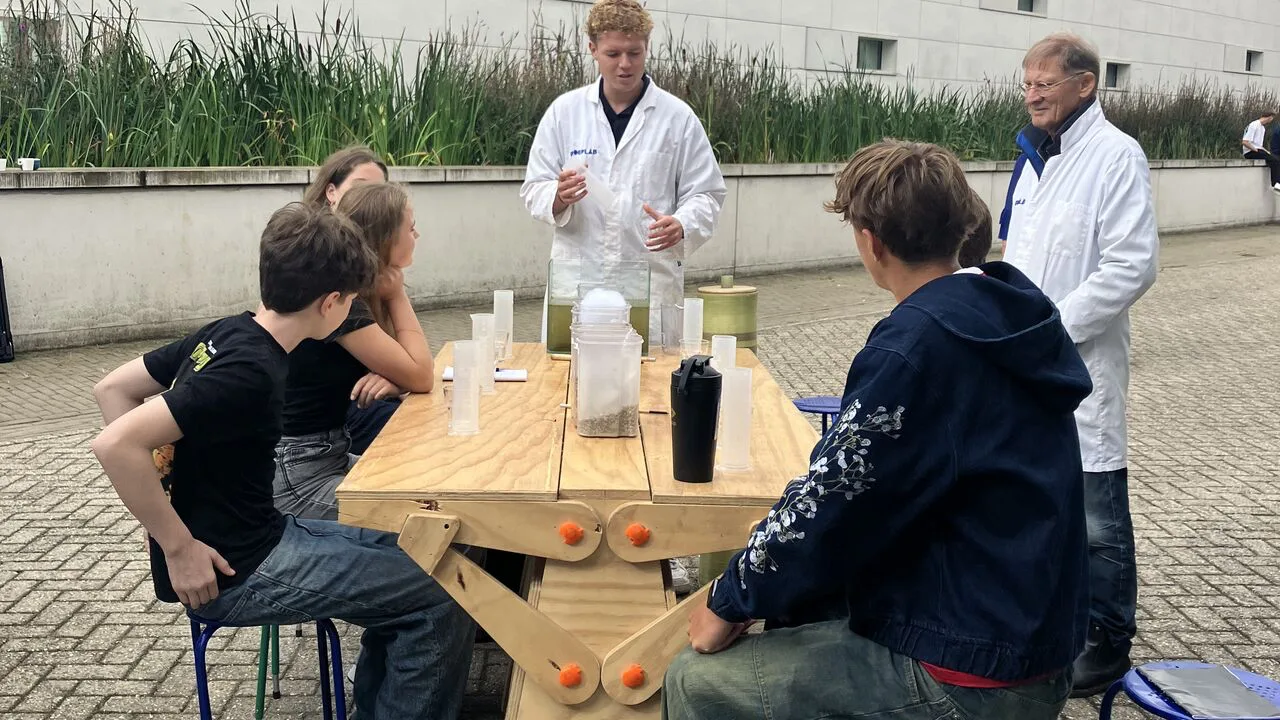 Scholieren doen een waterzuiveringsproef aan een houten tafel buiten bij PWN